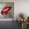 Pop art piece featuring glossy red lips against a textured silver background, displayed on a modern wall.
