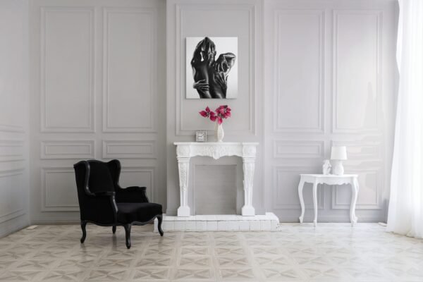 Black-and-white figurative painting of an embrace displayed above a white fireplace in a classic, elegant interior with a black armchair and floral decor.