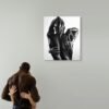 Black-and-white figurative painting of an embrace displayed on a wall, with a couple embracing in front of it, symbolizing human connection and art.