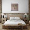 Modern face art painting of a woman’s surreal portrait displayed in a rustic bedroom with wooden beams and neutral decor.
